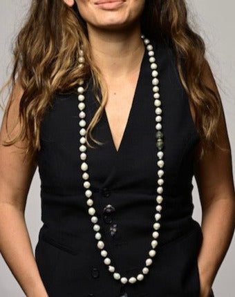 A person wearing a black sleeveless top and a long beige necklace with a pendant.