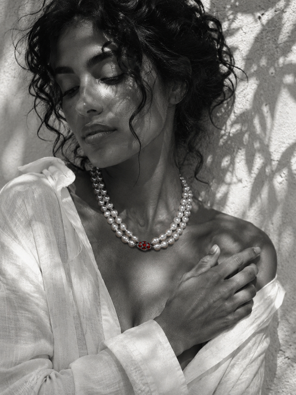 Long baroque pearl necklace doubled at collarbone length, garnet ornament in deep red at center, worn on a model in white linen, Mediterranean light