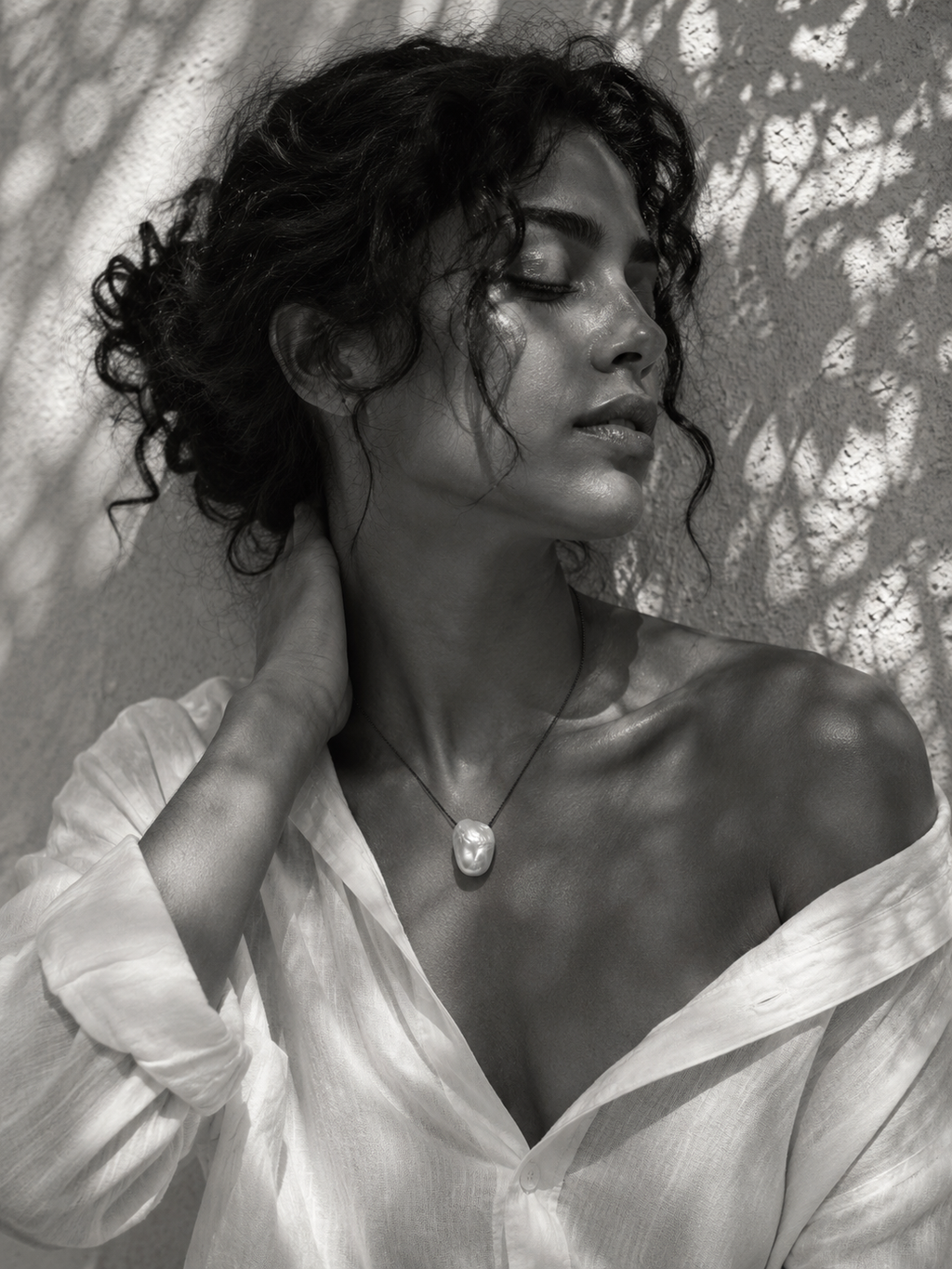 Baroque pearl pendant necklace on oxidized chain worn at the sternum, Mediterranean light and olive leaf shadows on whitewashed wall
