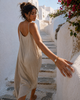 Arabelle bracelet by JLL Pearl — Mediterranean woman in sand linen dress walking up narrow Cycladic steps, hand trailing along whitewashed wall, gold bead and baroque pearl bracelet clearly visible on wrist, bougainvillea above