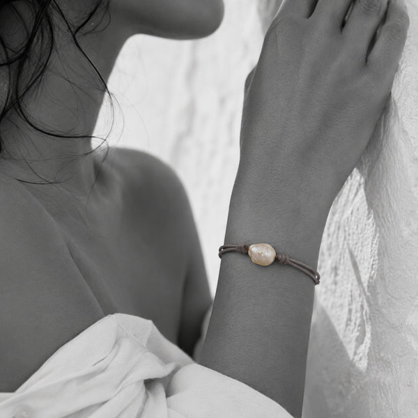 Black and white portrait of a baroque pearl bracelet on knotted cord against a stone wall — JLL Pearl