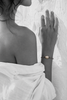 Banggai bracelet by JLL Pearl — black and white portrait, Mediterranean woman, hand flat against rough white Greek wall, selective colour on grey satin cord with single large baroque freshwater pearl