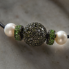 Close-up of Bao necklace central connector, dark diopside pavé ball flanked by two vivid green peridot rondelles, white freshwater pearls on black satin cord, JLL Pearl