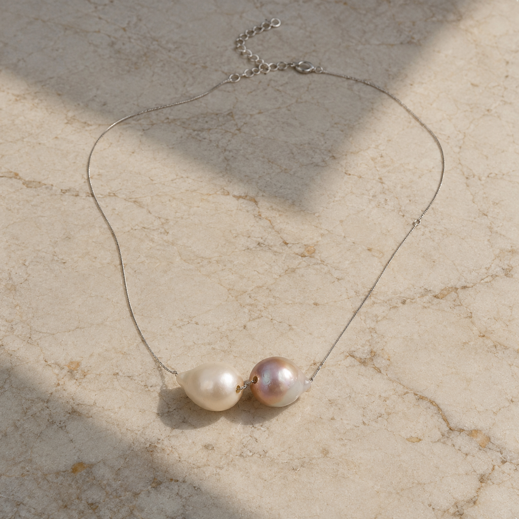 Bocca baroque pearl necklace silver chain flatlay on aged marble, two baroque freshwater pearls in cream and pink-mauve with fine silver chain and lobster clasp visible, natural sunlight, JLL Pearl