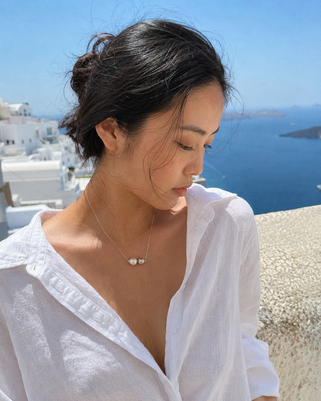 Bocca baroque pearl necklace silver chain worn by Asian model on Greek island terrace, full color, cream and pink-mauve pearls against Aegean backdrop and white linen shirt, JLL Pearl