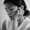Bocca bracelet by JLL Pearl — black and white portrait, East Asian woman, hand against cheek, selective colour on grey macramé cord with baroque white pearl and navy blue sapphire teardrop