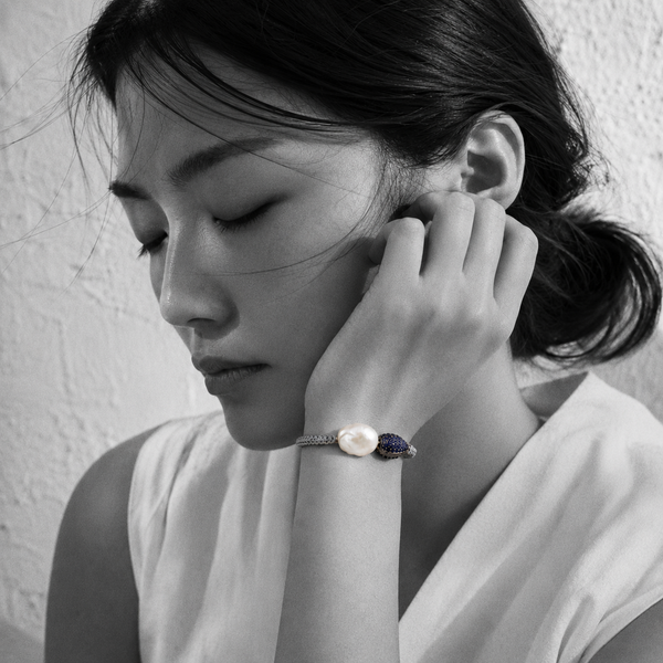 Bocca bracelet by JLL Pearl — black and white portrait, East Asian woman, hand against cheek, selective colour on grey macramé cord with baroque white pearl and navy blue sapphire teardrop