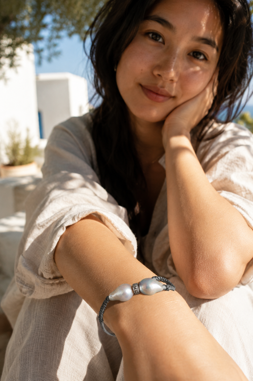 Butterfly macramé bracelet baroque grey pearls worn — Asian woman sitting, Greek village, natural Mediterranean light