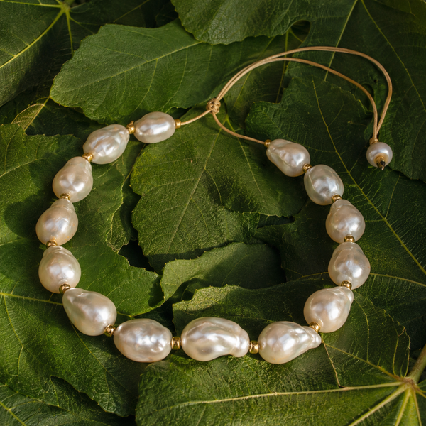 Eden baroque pearl gold flower choker arranged on fresh Mediterranean fig leaves, large baroque freshwater pearls with ornate gold-plated flower caps on braided gold satin cord, colour flat lay, handmade by JLL Pearl