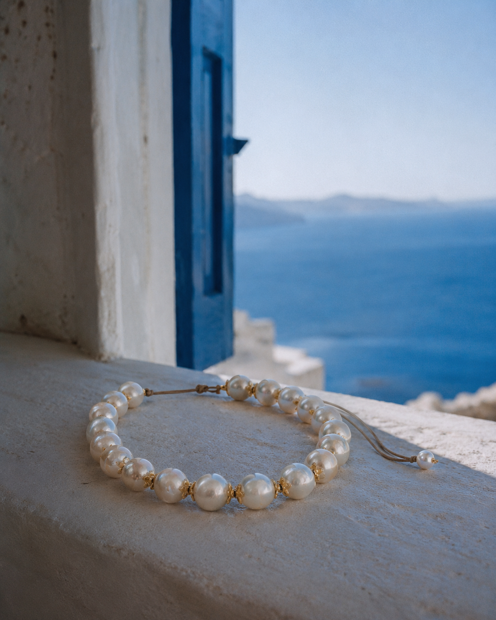 Ella round pearl gold flower choker on whitewashed stone windowsill with Aegean Sea and blue shutter in background

