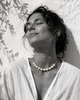 Ella round pearl gold flower choker worn at the throat, woman head tilted back eyes closed in Mediterranean sun against whitewashed wall