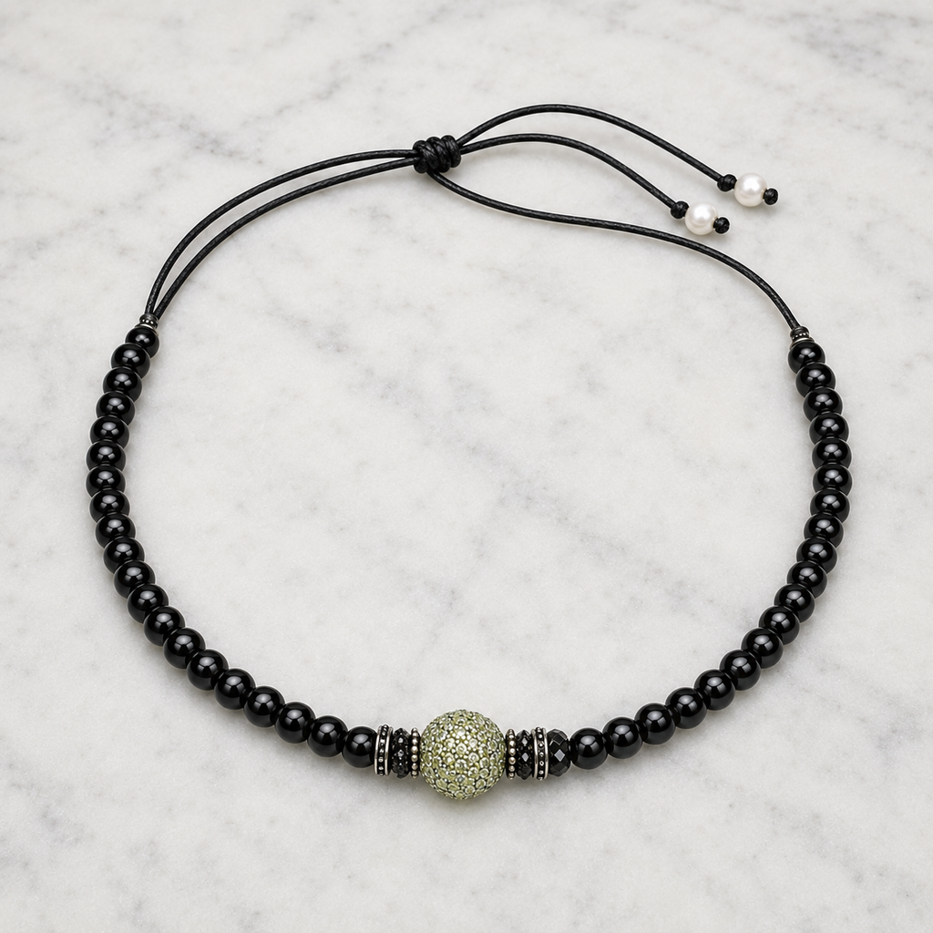 Hydra black onyx peridot necklace flatlay on white marble, black onyx beads on black satin lasso cord, central pavé peridot sphere flanked by spinel toupies, freshwater pearl finials visible