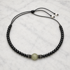 Hydra black onyx peridot necklace flatlay on white marble, black onyx beads on black satin lasso cord, central pavé peridot sphere flanked by spinel toupies, freshwater pearl finials visible