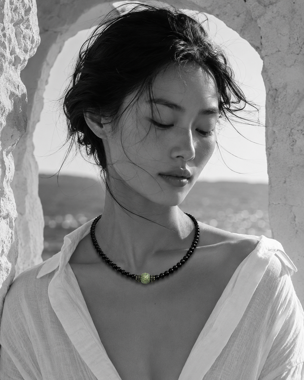Hydra black onyx peridot necklace worn by Asian model in whitewashed stone arch, eyes closed, white linen shirt, peridot sphere in natural celadon green, handmade by JLL Pearl