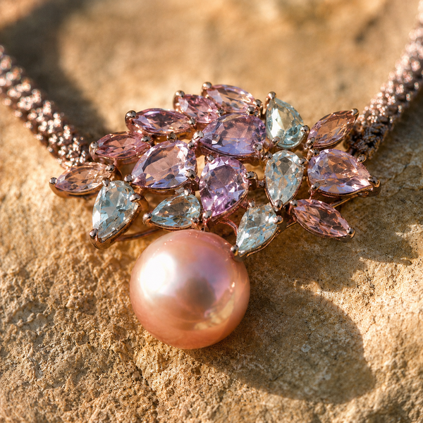 Macro close-up of the Karla bracelet — asymmetric cluster of pale amethyst and aquamarine marquise and pear-cut stones in rose gold settings, round pink baroque freshwater pearl pendant hanging below, on warm sandstone in raking sunlight — JLL Pearl