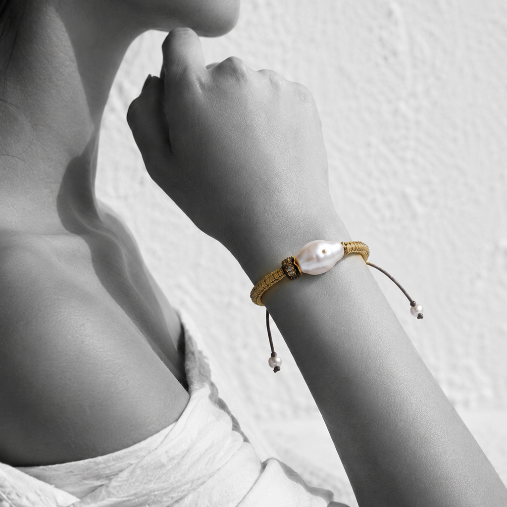 Black and white portrait of a baroque pearl bracelet on woven gold cord with pearl-tipped ties — JLL Pearl