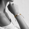 Black and white portrait of a baroque pearl bracelet on woven gold cord with pearl-tipped ties — JLL Pearl