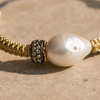 Close-up of Kea bracelet dark metal pavé rondelle with white topaz stones beside baroque freshwater pearl, gold macramé cord
