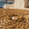 Kea baroque pearl gold macramé bracelet on woven seagrass mat, warm afternoon Mediterranean light