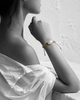 Kea baroque pearl gold macramé bracelet on wrist raised near face, black and white portrait with selective colour on bracelet