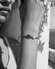 Killi bracelet worn on wrist — raw emerald in gold bezel and baroque freshwater pearl on grey macramé cord, black and white photograph with bracelet in color, Greek white wall background