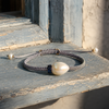 Killini bracelet — grey macramé cord, cream-white baroque pearl and blue sapphire rondelle — resting on aged blue-grey painted wood in Mediterranean light — JLL Pearl