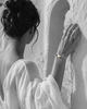 Killini grey macramé bracelet with baroque pearl and blue sapphire toupie on a Mediterranean woman's wrist, raised against a white Greek archway — JLL Pearl