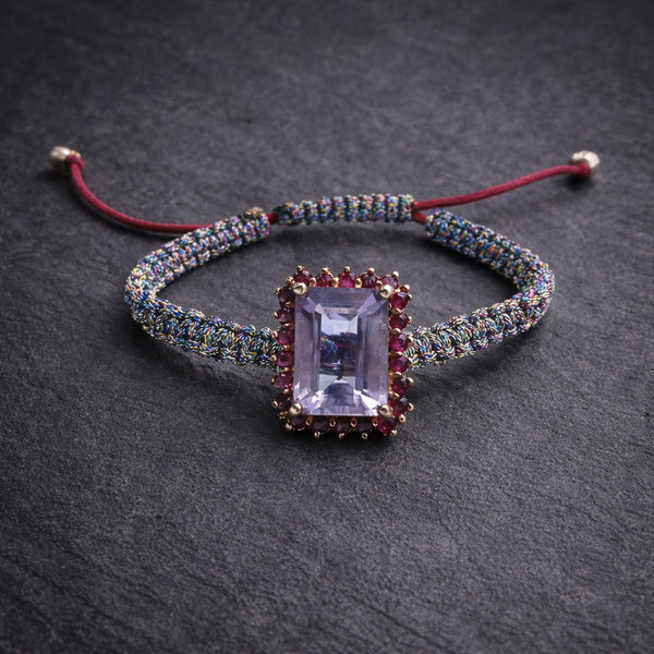 Kos amethyst topaz woven bracelet — flatlay on dark grey slate: pale lavender emerald-cut amethyst, pink topaz halo with gold beads, iridescent multicolour macramé cord — JLL Pearl