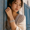 Lalibella bracelet worn on the wrist of a young woman leaning against a blue painted Greek door — three rows of round white freshwater pearls with grey satin knotting, central 8-pointed champagne diamond star in oxidized silver — JLL Pearl