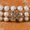 Macro close-up of the Lalibella bracelet — three rows of round white freshwater pearls individually knotted in grey satin cord, central 8-pointed champagne diamond star in oxidized silver, on warm terracotta stone — JLL Pearl