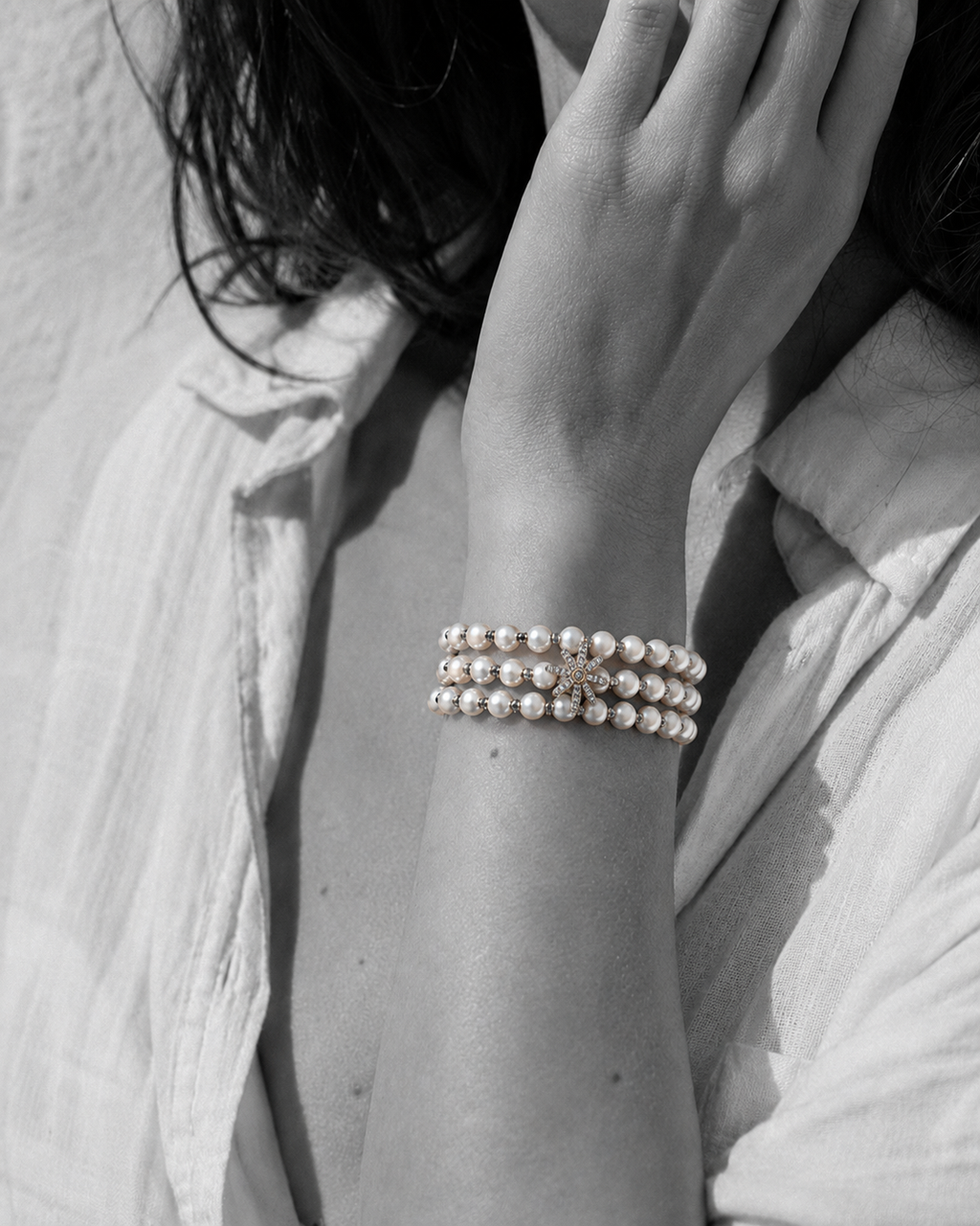 Three-strand pearl bracelet with grey macramé cord and silver star on wrist, black and white portrait