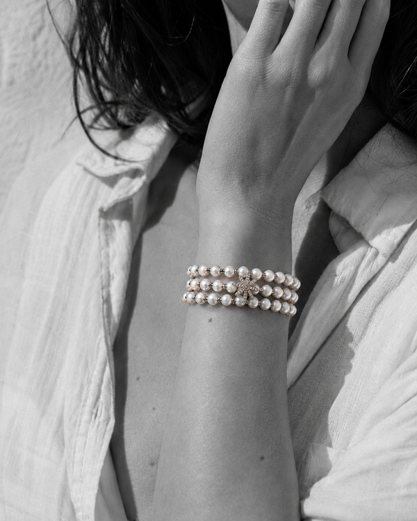 Three-strand pearl bracelet with grey macramé cord and silver star on wrist, black and white portrait