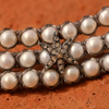 Macro close-up of Lalibella: grey macramé cord weaving over and under each pearl, silver star with champagne diamonds