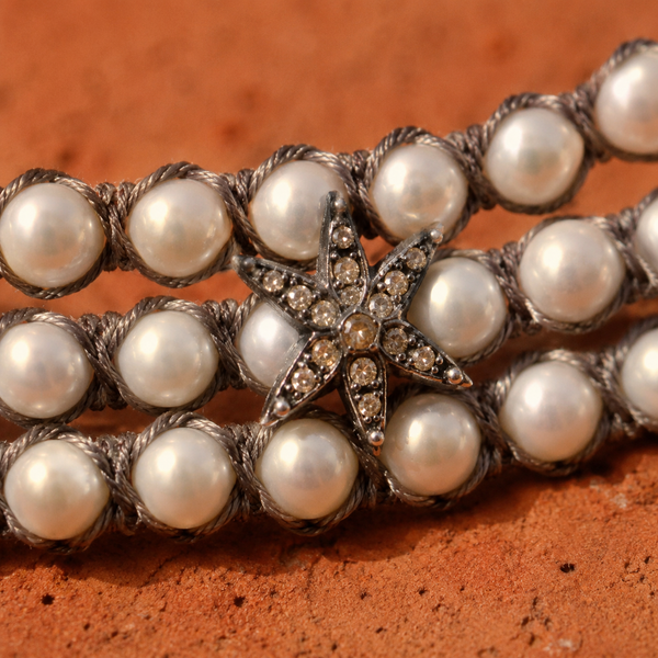 Macro close-up of Lalibella: grey macramé cord weaving over and under each pearl, silver star with champagne diamonds