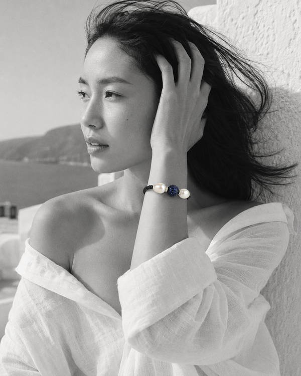 Manhattan bracelet by JLL Pearl — black and white portrait, East Asian woman, wind in hair, selective colour on dark macramé cord, baroque white pearls and deep blue sapphire ball