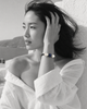 Manhattan bracelet by JLL Pearl — black and white portrait, East Asian woman, wind in hair, selective colour on dark macramé cord, baroque white pearls and deep blue sapphire ball