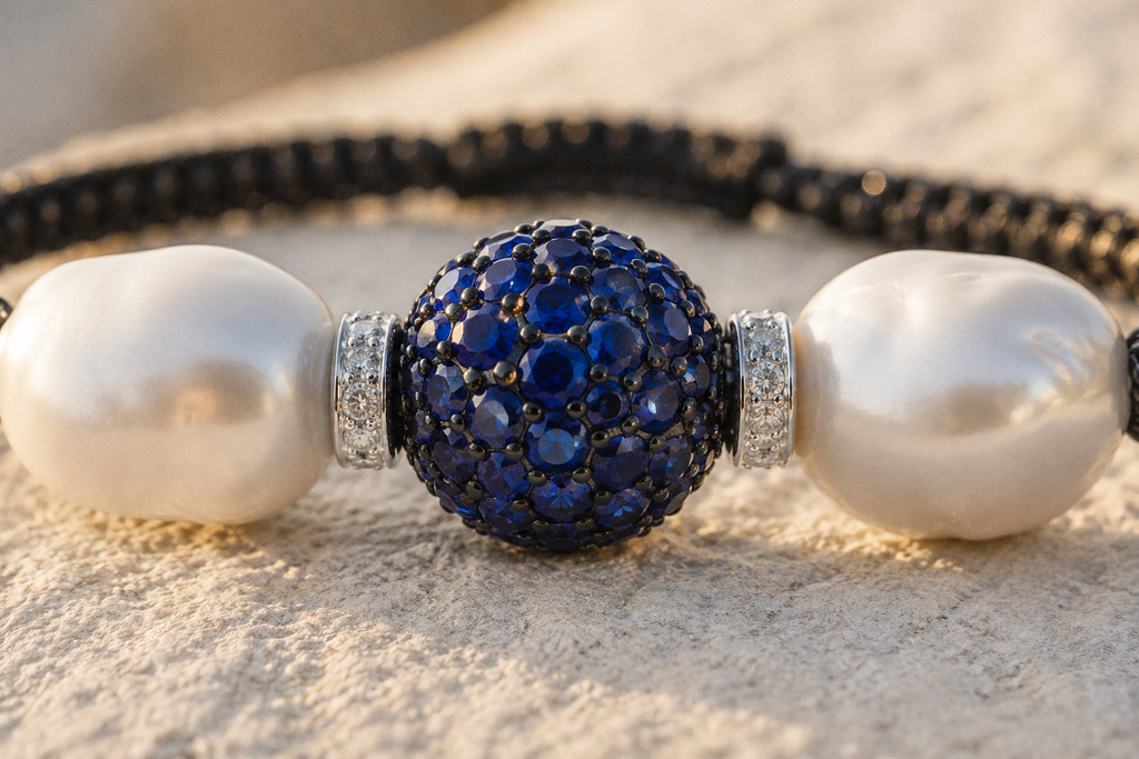 Manhattan bracelet by JLL Pearl — macro close-up on deep navy blue pavé sapphire ball on silver, flanked by diamond bicones and large baroque white freshwater pearls, warm stone surface