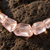 Mani rose amethyst pyrite necklace macro detail, faceted rose amethyst chunks with internal light refraction, gold-plated rondelle beads on dark volcanic stone surface, JLL Pearl