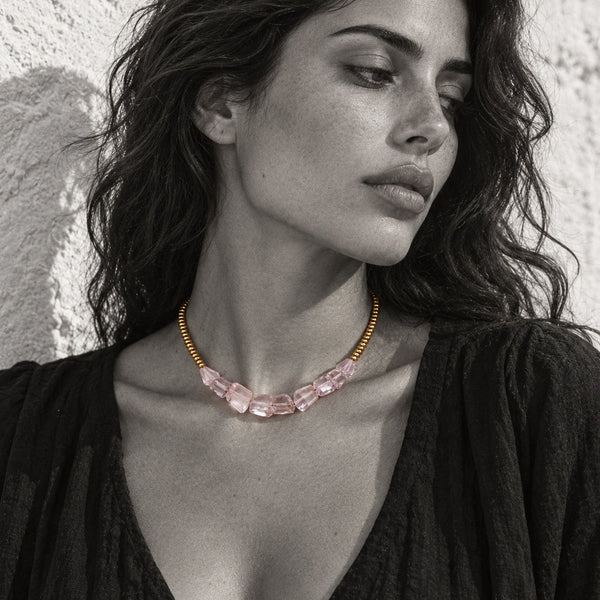 Mani rose amethyst pyrite necklace worn by a Mediterranean woman, black and white editorial portrait, selective colour on faceted rose amethyst chunks and gold-plated beads, white plastered wall background, handmade by JLL Pearl