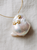 Close-up of Mila baroque pearl pendant with three gold star ornaments set with white topaz, iridescent freshwater baroque pearl on pale linen, JLL Pearl