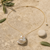Mila baroque pearl white topaz gold necklace arranged on pale weathered stone with green leaves and a smooth white stone, JLL Pearl