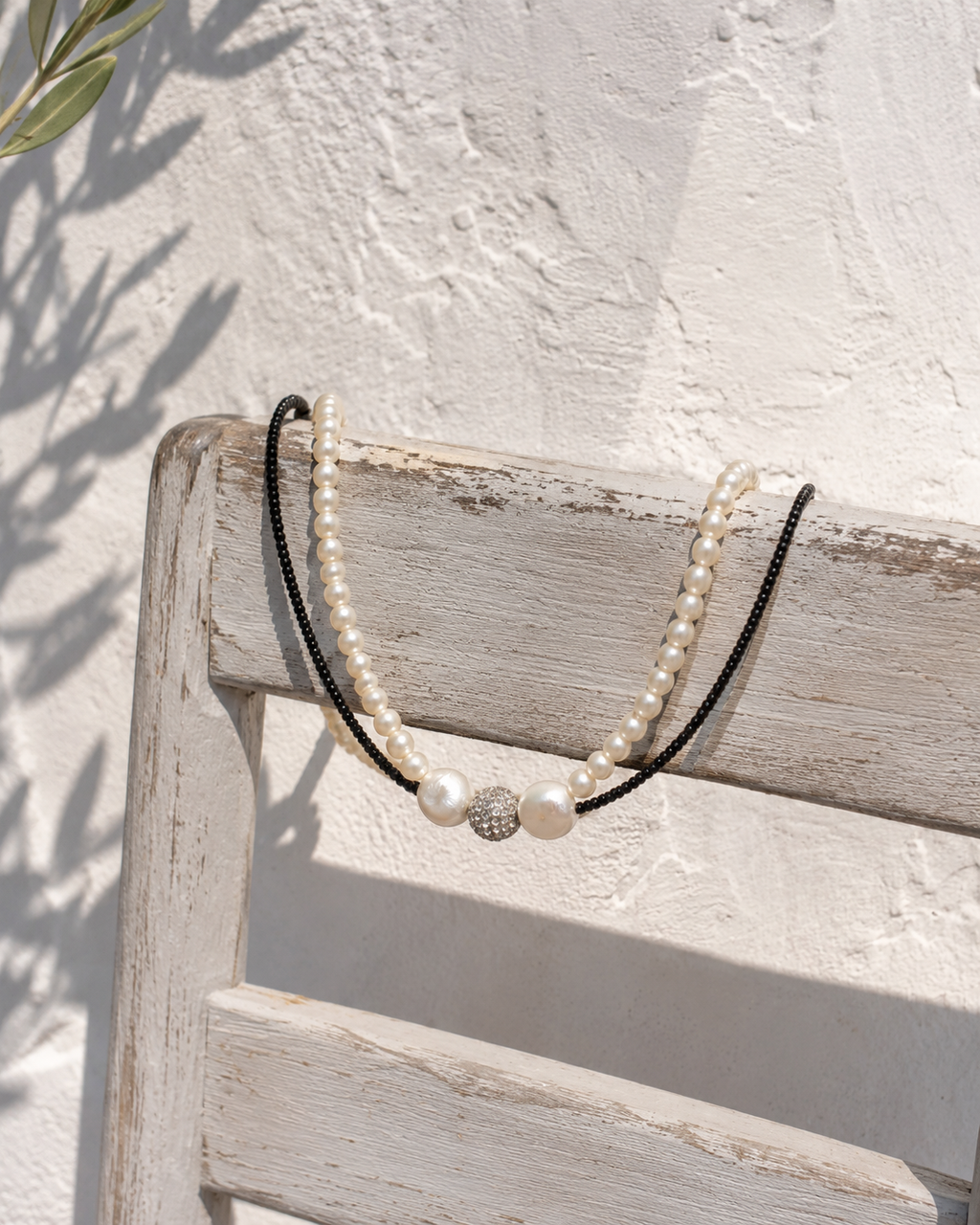 Mina pearl spinel necklace draped over a whitewashed wooden chair against a Greek whitewashed wall