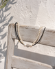 Mina pearl spinel necklace draped over a whitewashed wooden chair against a Greek whitewashed wall