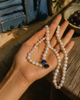 Nati pearl necklace lapis lazuli sapphire gold held in an open feminine palm, Mediterranean background with blue shutters and dark olives, JLL Pearl