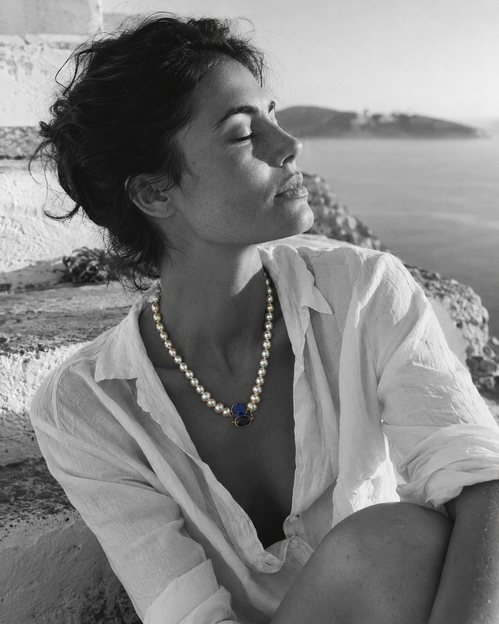 Nati pearl necklace lapis lazuli sapphire gold worn by a woman on white marble steps by the Aegean Sea, black and white editorial photograph, JLL Pearl