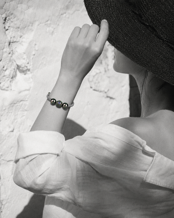 Black and white portrait of woman adjusting hat, Paros Tahitian pearl macramé bracelet in selective colour on wrist, Greek wall