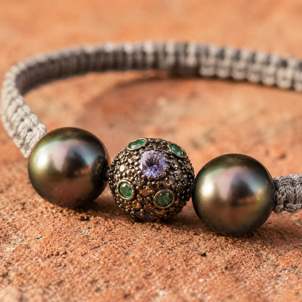 Macro close-up of Paros bracelet central stone ball with semiprecious stones, flanked by two dark Tahitian pearls on grey macramé cord