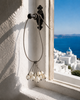 Peipei baroque pearl cluster necklace hanging from a Greek window latch, Santorini white architecture and blue Aegean sea in the background, warm Mediterranean light, colour photograph, JLL Pearl