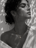 Romy white topaz pendant hematite necklace worn at the collarbone, pear-cut topaz in gold halo setting on gold hematite beaded chain, black satin cord, olive leaf shadows on whitewashed wall, handmade by JLL Pearl