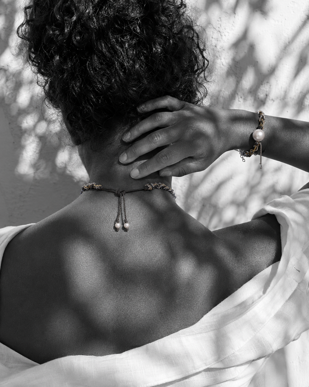 Samos braided silver gold chain pearl choker worn from behind, sliding knot closure with pearl finials at nape, matching Samos bracelet on wrist, olive leaf shadows on whitewashed wall, handmade by JLL Pearl
